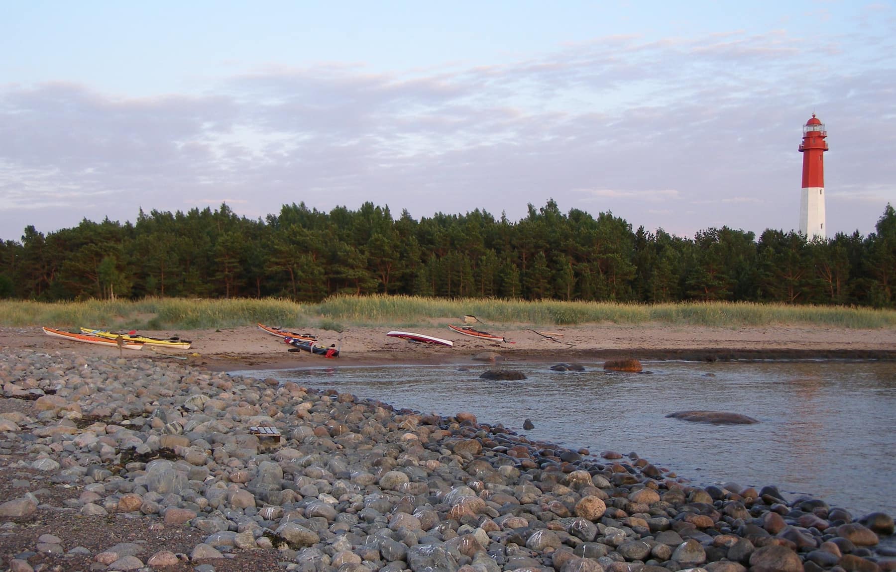 The red-and-white Naissaar lighthouse above the forest and the stony northern shore of the island