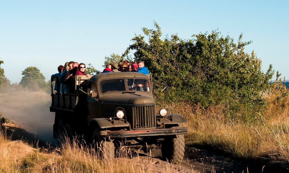 Visitors riding in the back of an old military truck on a sandy track on Naissaar